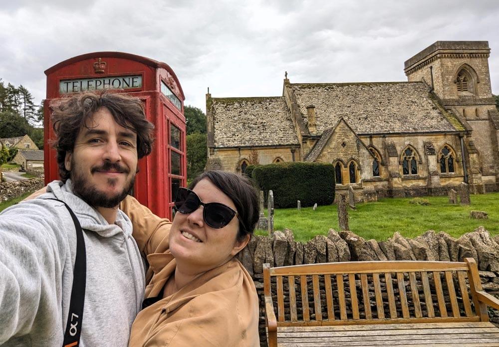 viaggiatori nei Cotswolds con una cabina rossa e una chiesa antica sullo sfondo